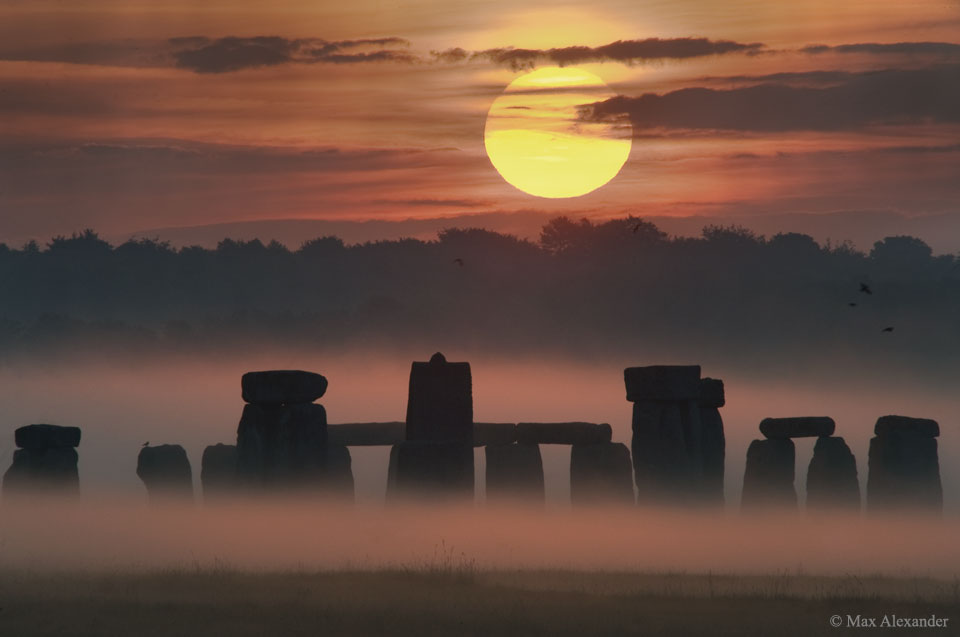 The picture shows the Sun rising over the blocks of Stonehenge. 
Please see the explanation for more detailed information.