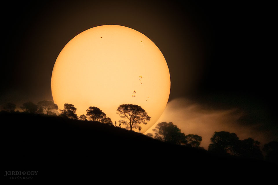 The picture shows the Sun rising over a hill 
in Perter, Spain, complete with sunspots and foreground trees.
Please see the explanation for more detailed information.