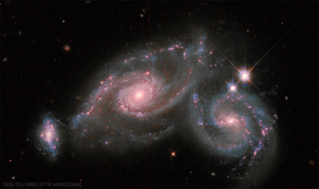 Two spiral galaxies are shown right next to each other, 
with a smaller distorted galaxy on the far left.
Please see the explanation for more detailed information.