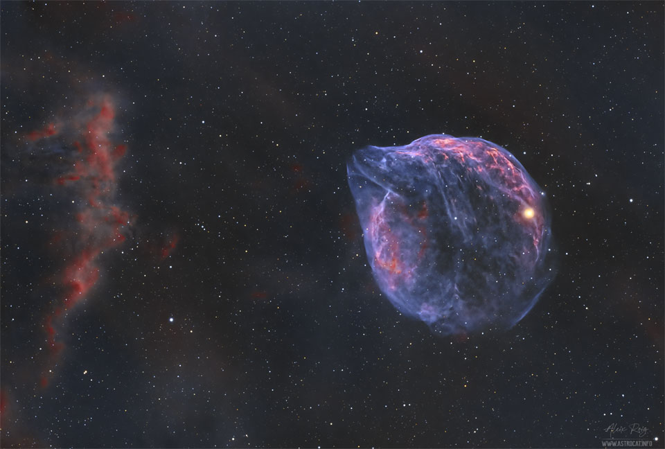 A star field is shown with ragged red clouds on 
the far left and a thin blue cloud with the outline
similar to the head of a dolphin to the right.
Please see the explanation for more detailed information.