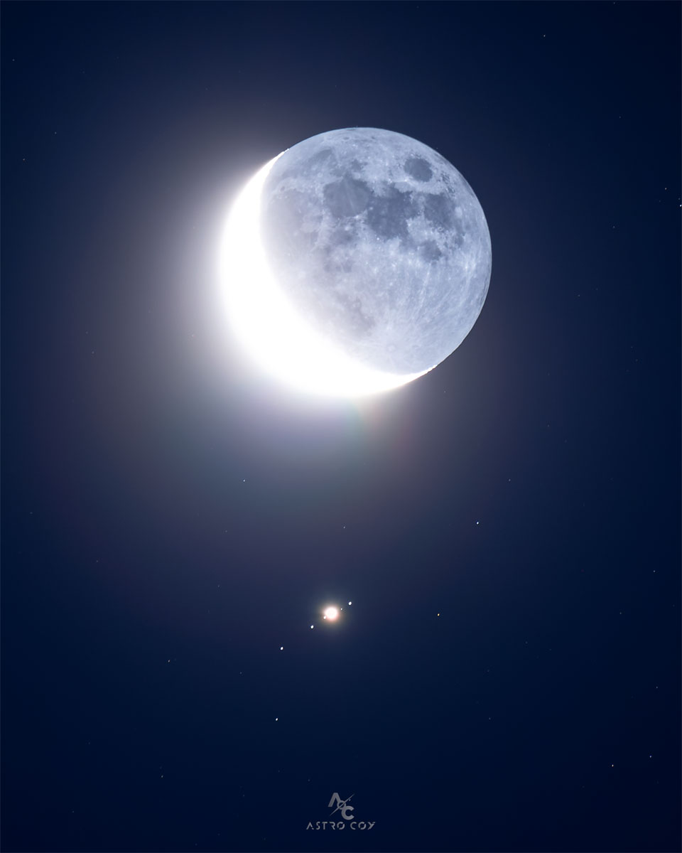 Earth Moon, in crescent phase, is seen just above the 
image center. Directly below is a bright spot surrounded by
four other spots, all in a row, which are all moons of
Jupiter.
Please see the explanation for more detailed information.