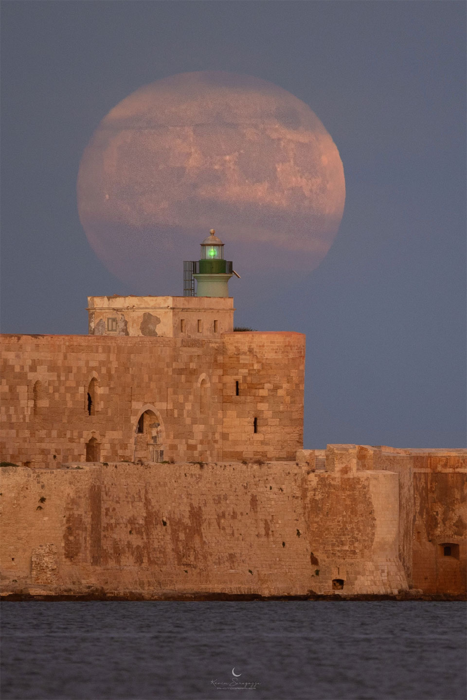 A large Moon is seen behind a historic stone structure. 
Please see the explanation for more detailed information.