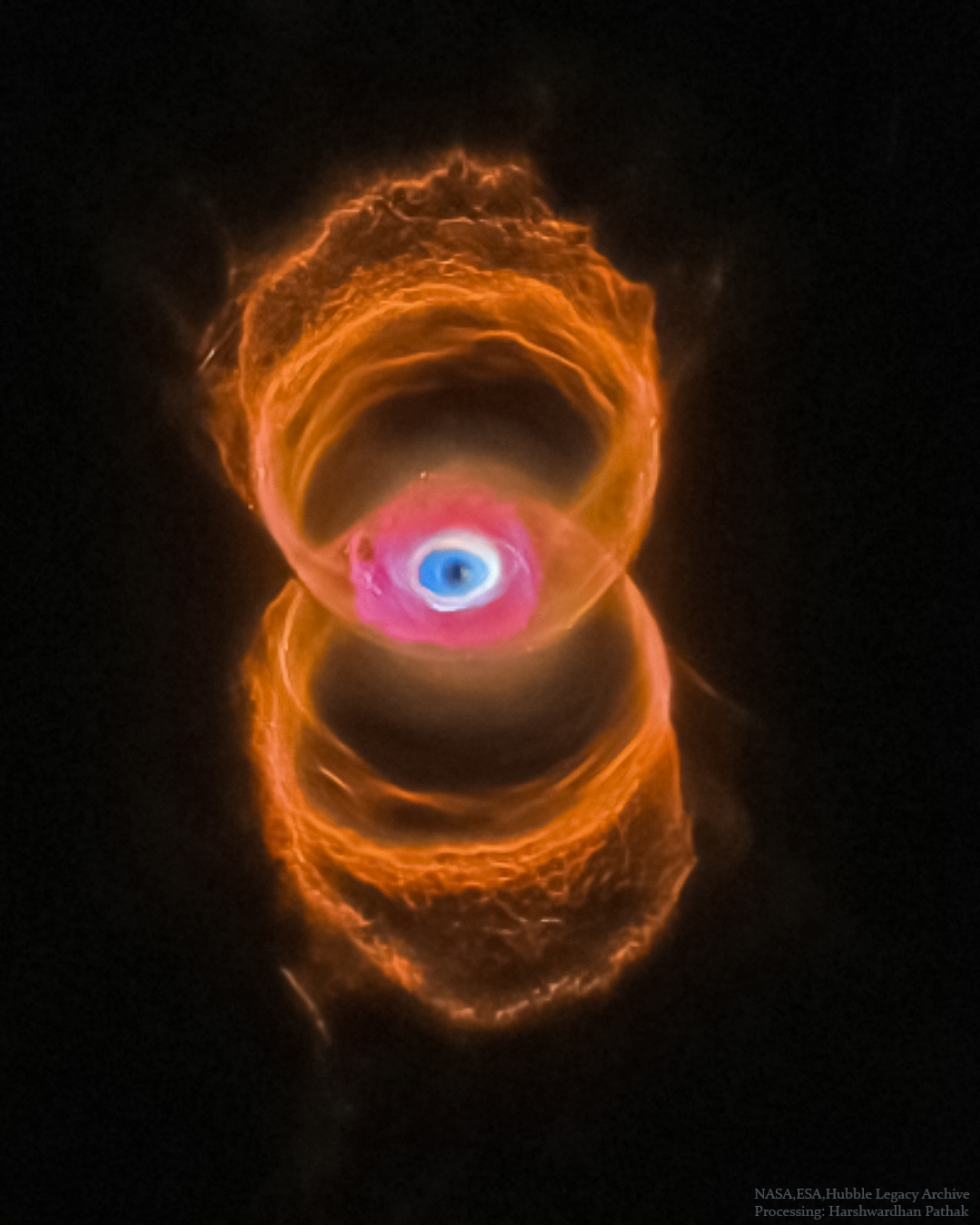A vertical planetary nebula is shown in orange around the 
outside but with a blue glow in the center. The outside is 
shaped like a tilted hourglass, while the inside appears similar
to an eye.
Please see the explanation for more detailed information.
