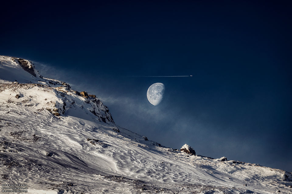 A mostly full moon is seen over a snowy sloping hill.
An airplane and contrail are seen just about the Moon.
Please see the explanation for more detailed information.