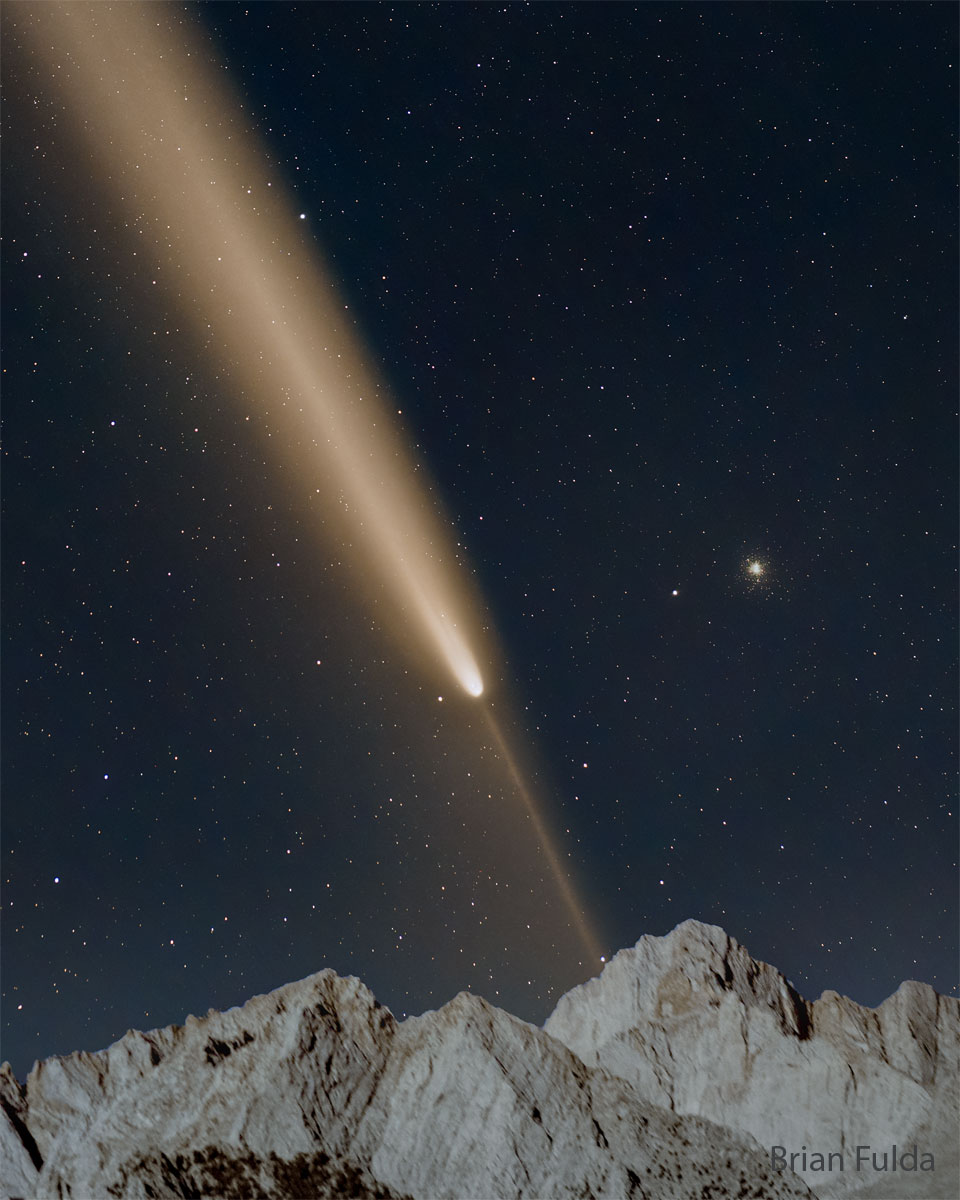 A starfield is shown with a bright comet. The main
tail of the comet points diagonally to the upper left, while
a thin anti-tail points to the lower right. Mountain peaks
are visible at the bottom in the foreground. 
Please see the explanation for more detailed information.