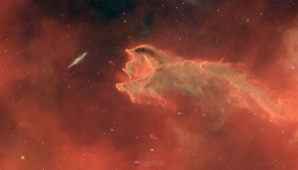 A cometary globule extends in front of a field of stars,
	  showing what seems like an open mouth towards a distant
	  galaxy in the background.
	  Please see the explanation for more detailed information.