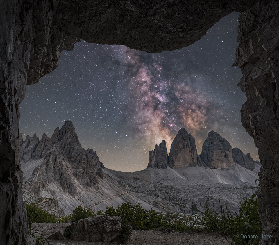 A starry sky is seen through a rectangular rock
opening. Three rocky peaks appear toward the right, while
other peaks appear toward the left. Rising above the 
right peaks is the central band of our Milky Way Galaxy.
Please see the explanation for more detailed information.