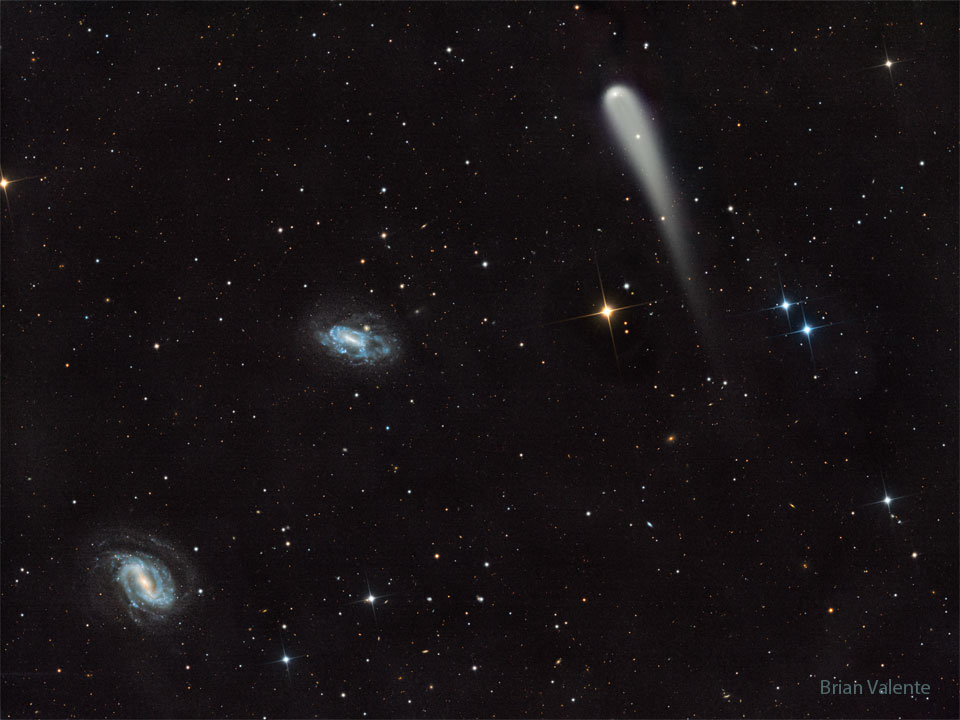 A picture shows a starfield with three prominent objects.
A blue spiral galaxy is on the lower left and another blue spiral
is just left of center. Toward the upper right is a light-colored
comet with a tail fading toward in the image bottom.
Please see the explanation for more detailed information.