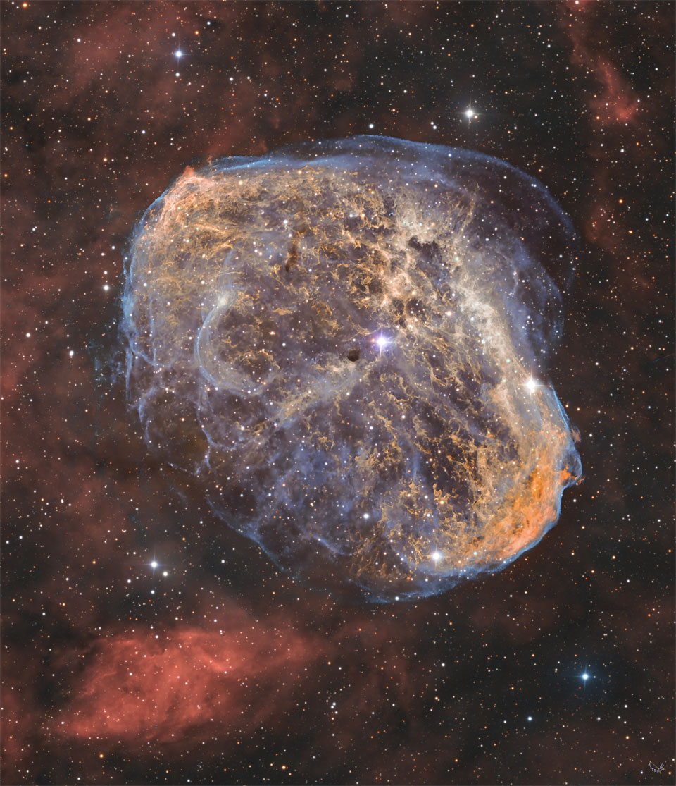 A starfield is shown with a unusual textured nebula
in the center colored in brown with blue trimmings. Diffuse
red nebula appear around the edges. In the center is an
opaque brown object. 
Please see the explanation for more detailed information.