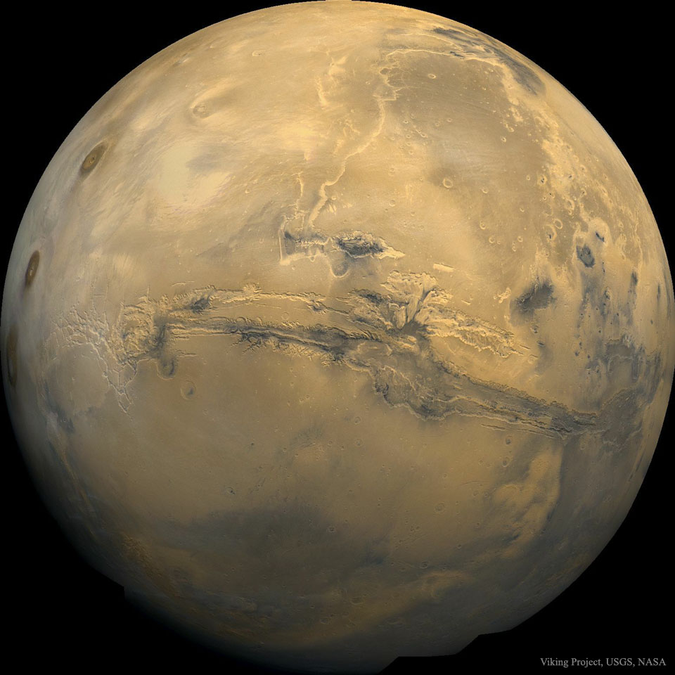 A picture of Mars is shown as a large orange globe.
Across the center of the planet a long canyon is visible. 
Please see the explanation for more detailed information.