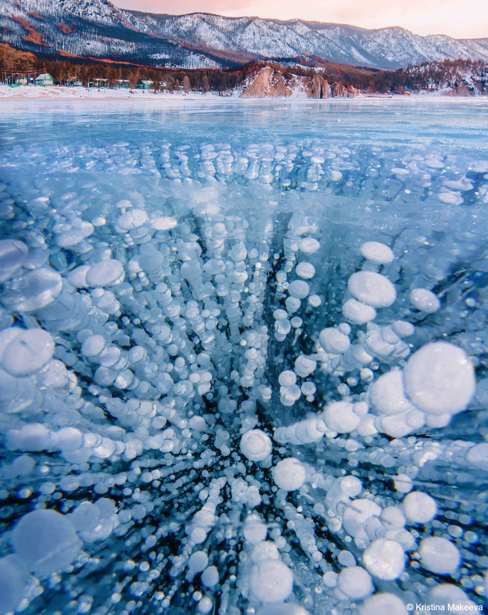 A frozen lake is shown that appears quite blue.
Many oval light-colored bubbles are frozen into the 
ice, many times in columns. 
Please see the explanation for more detailed information.