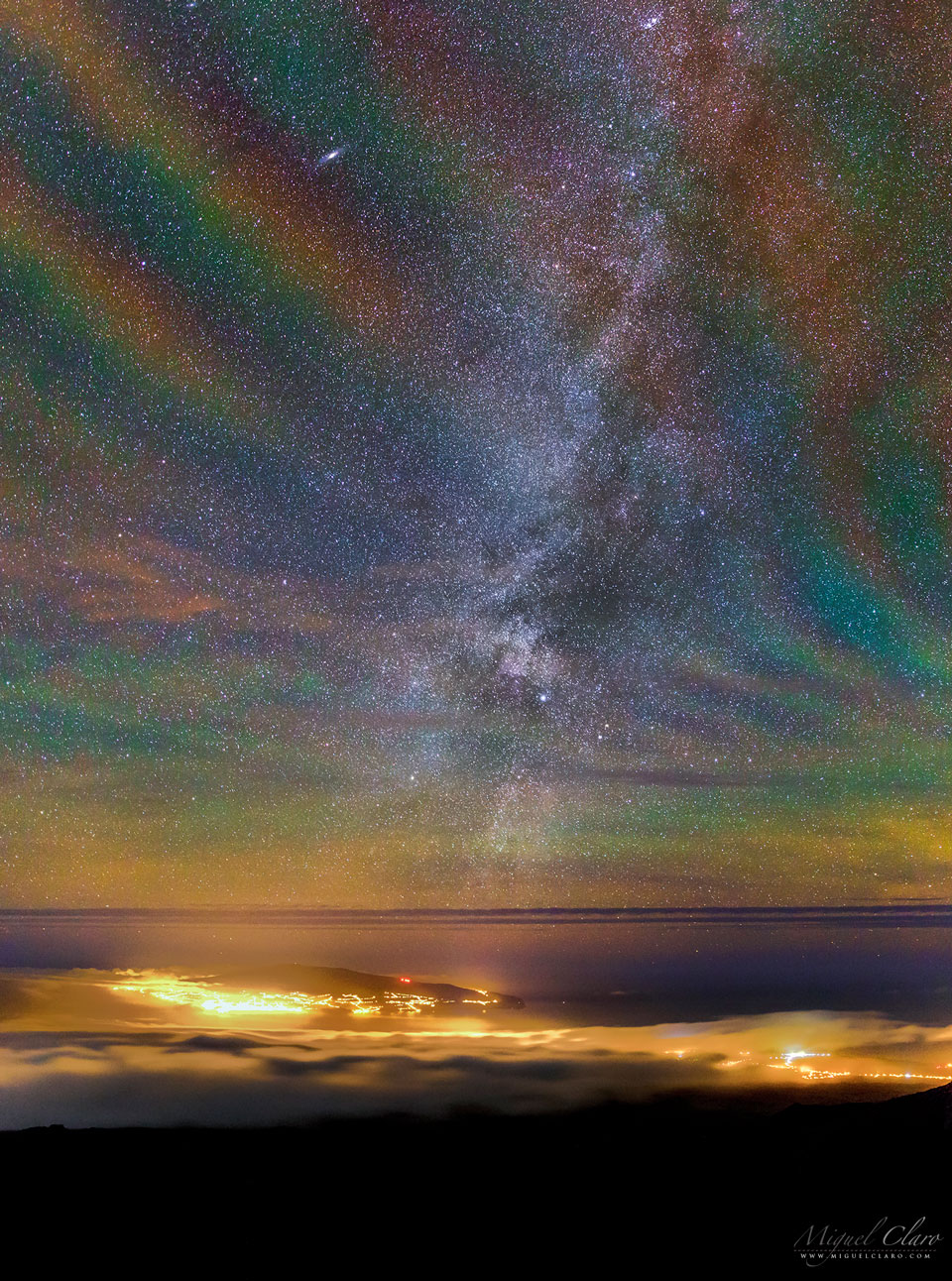 A starfield is seen over water, clouds, and the lights of
a city below. The starfield is oddly not black, but shows a 
repeating assortment of transparent colors diagonally from the lower
left to the upper right. 
Please see the explanation for more detailed information.
