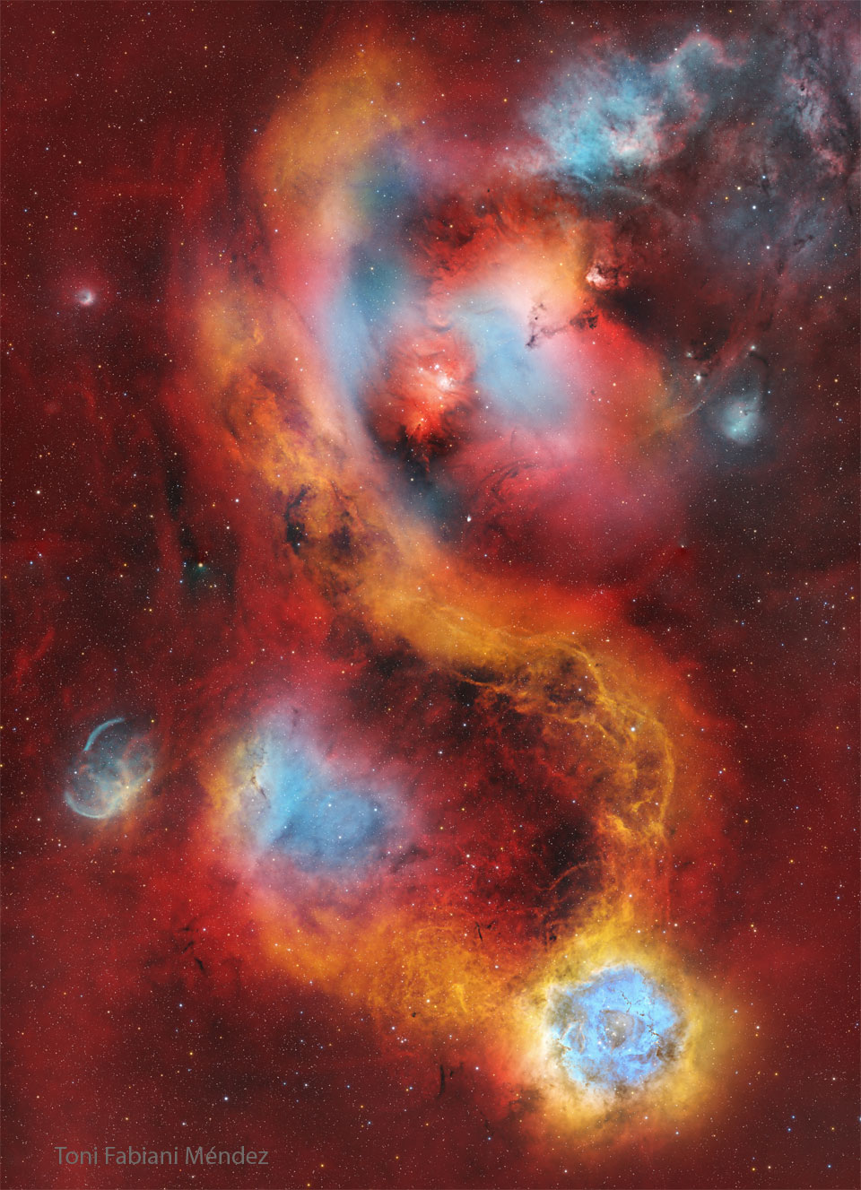 A starfield is covered with a light red glow. Several
nebulas are seen near the center. The famous Rosetta nebula
appears in blue and white near the image bottom. 
Please see the explanation for more detailed information.