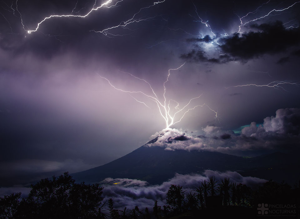 A volcano is shown with its peak in the midst of 
purple clouds. Lightning appears to come out of the 
top of the volcano in multiple paths into the upper sky.
Please see the explanation for more detailed information.
