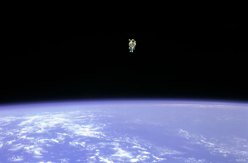 An astronaut is seen hovering over the Earth. In the 
top part of the image, the astronaut is seen against the 
darkness of space. In the lower part of the image, the
Earth is bright blue with white clouds.
Please see the explanation for more detailed information.