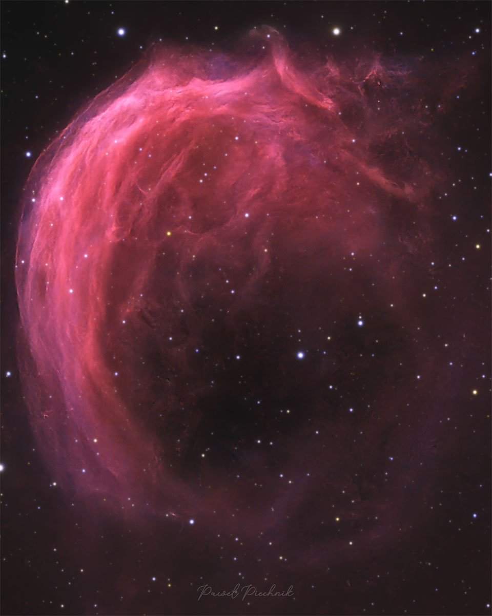 A starfield has a bright pink swirling nebula 
in it. The top part of the nebula shows much detail,
while the bottom part is mostly open.
Please see the explanation for more detailed information.