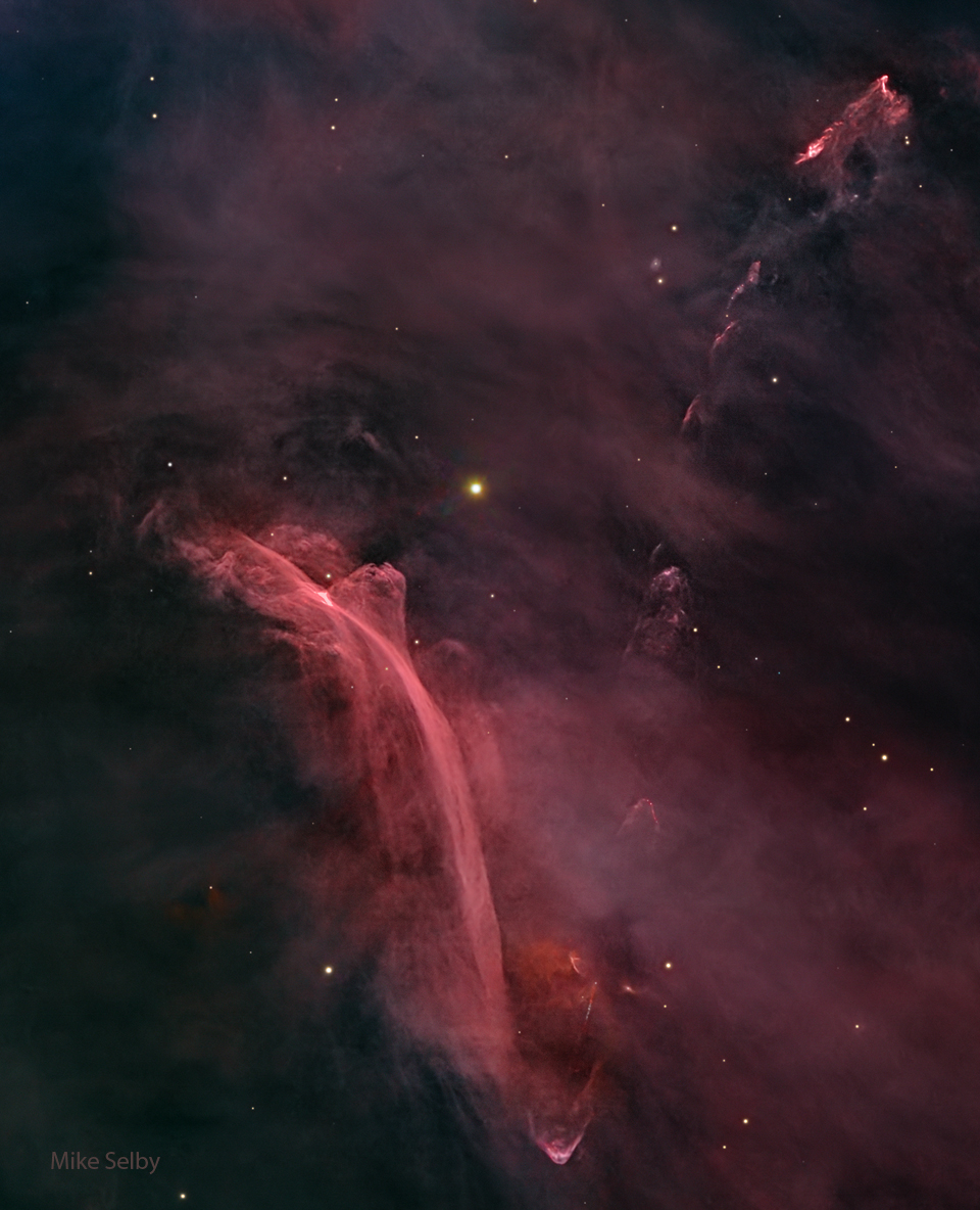 A starfield filled with a diffuse red glow has an
unusual nebula on the lower left. The nebula has bright
red filaments that curve down and appear to be reminiscent of
a waterfall on Earth. 
Please see the explanation for more detailed information.