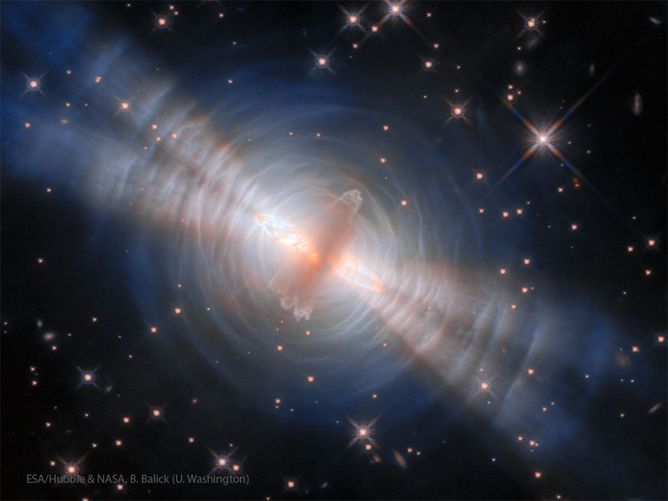 A starfield is shown with an unusual orange object in the center.
Surrounding this object are blue rings and four thick jets. 
Please see the explanation for more detailed information.